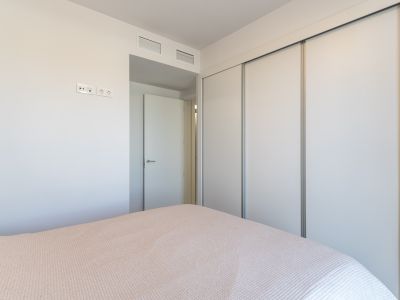 Vista de dormitorio con un amplio armario empotrado de puertas correderas blancas. La pared presenta tomas eléctricas modernas y rejillas de ventilación integradas sobre la puerta adyacente.