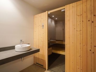 Zona de vestuario con un elegante lavabo sobre encimera flotante de diseño y la entrada a la sauna, con puerta de madera y cristal, parte del centro social.