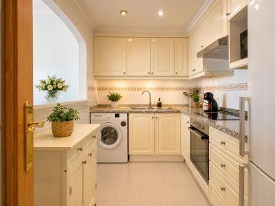 Cocina funcional con armarios crema, encimeras de granito y electrodomésticos integrados. Un pasaplatos arqueado y una puerta de madera añaden carácter al espacio.