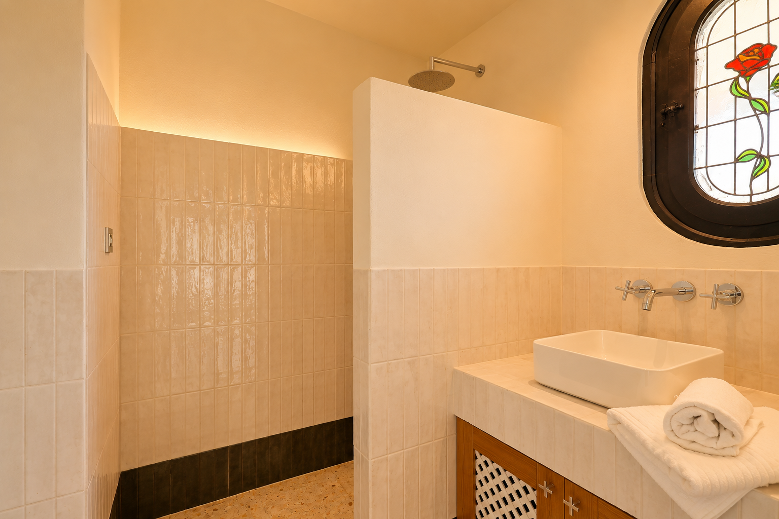 Baño moderno con ducha a ras de suelo, rociador de lluvia y luz LED indirecta. Lavabo sobre encimera de azulejos y una distintiva ventana ovalada de vidrieras con motivo de rosa.