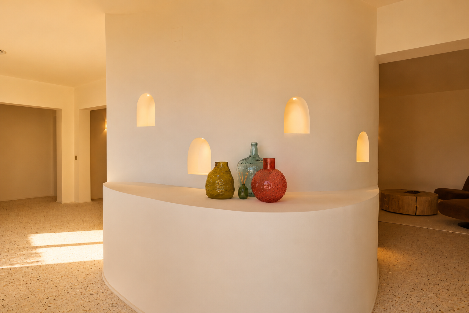 Pared divisoria curva con cuatro nichos arqueados iluminados y estante integrado que exhibe jarrones decorativos, sobre suelo de terrazo.