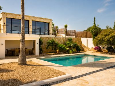 El exterior aterrazado de la villa presenta una piscina rectangular con pavimento de piedra irregular, un comedor exterior cubierto y fachada de piedra con amplios ventanales.