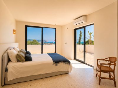 Luminoso dormitorio con suelo de terrazo claro y grandes puertas correderas de cristal que dan a una terraza privada. Ofrece amplias vistas al mar y la costa lejana.