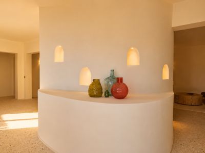 Pared divisoria curva con cuatro nichos arqueados iluminados y estante integrado que exhibe jarrones decorativos, sobre suelo de terrazo.