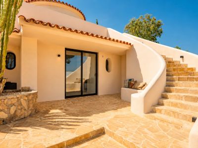 Patio exterior con pavimento de piedra irregular en tonos cálidos, escalera curva y un gran cactus. Incluye puerta corredera de cristal y banco integrado en la pared de estuco.
