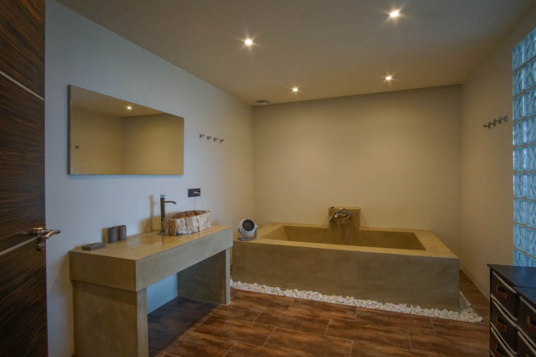 Baño moderno con lavabo de madera rústica sobre encimera de hormigón, bañera integrada y pared de bloques de vidrio.