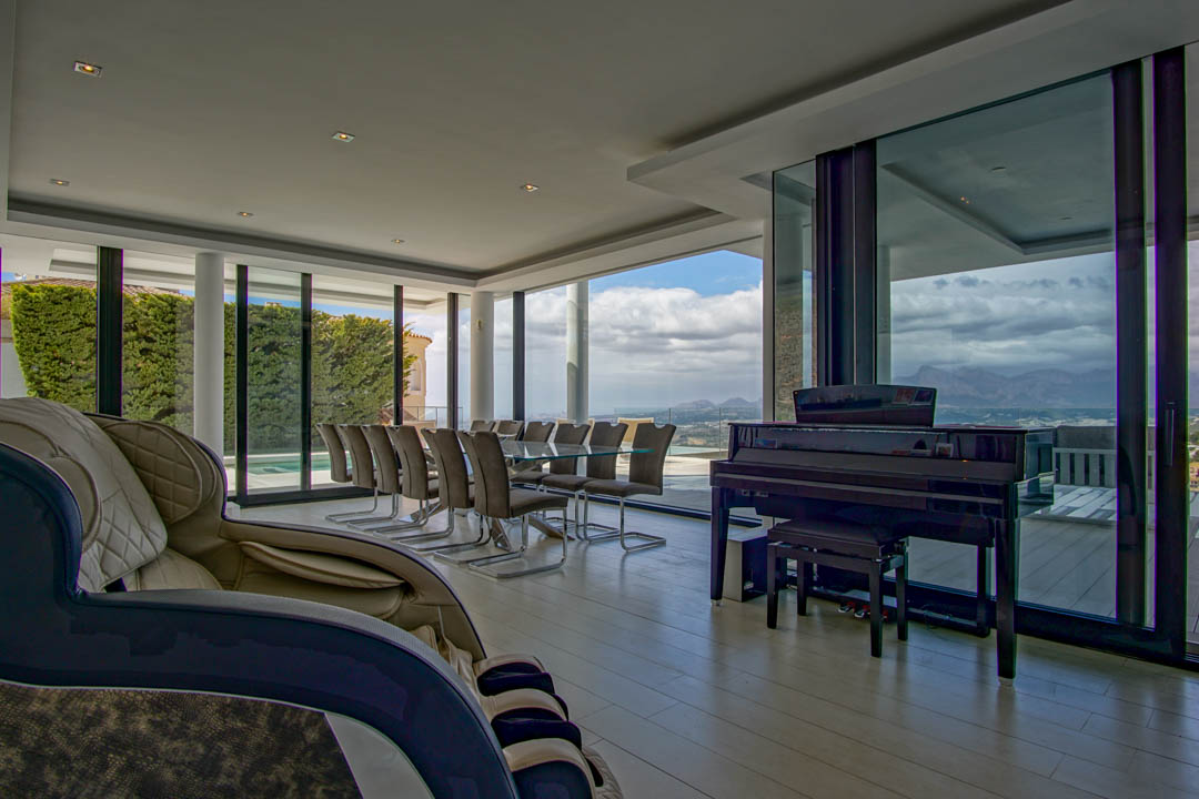 Espaciosa sala de estar y comedor con mesa de cristal para diez, piano de cola y sillón de masaje. Grandes ventanales ofrecen vistas panorámicas a la montaña y al paisaje.