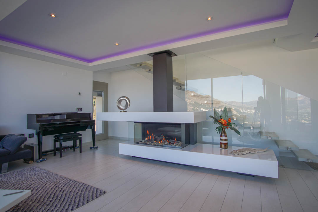 La elegante sala de estar presenta una moderna chimenea de gas transparente, un piano de cola y una escalera de cristal, con vistas a la montaña.