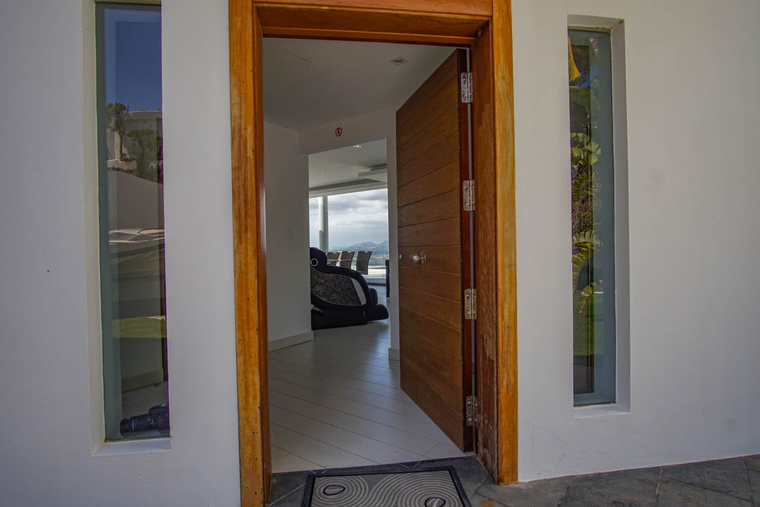 La entrada principal abierta revela una puerta de madera panelada y marco, flanqueada por ventanas verticales, con una visión del interior moderno y vistas a la montaña.