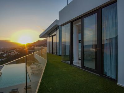Amplia terraza con piscina infinita, tarima de madera y barandilla de cristal, ofreciendo vistas panorámicas al atardecer sobre montañas y valle.