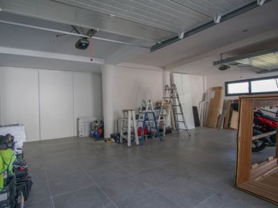Amplio garaje con suelo de baldosas grises y paredes blancas. Incluye dos mecanismos de puerta automática, ventanas horizontales para luz natural y espacio de almacenamiento con puertas correderas.