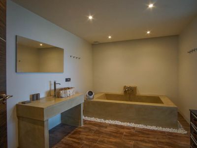 Baño moderno con lavabo de madera rústica sobre encimera de hormigón, bañera integrada y pared de bloques de vidrio.