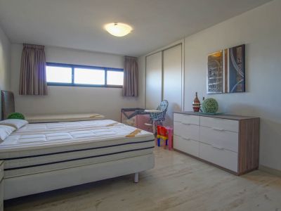 Dormitorio luminoso con una cama de dos colchones, suelo de madera clara y una ventana horizontal alargada. Incluye un armario blanco de puertas correderas y una cómoda moderna con arte abstracto.