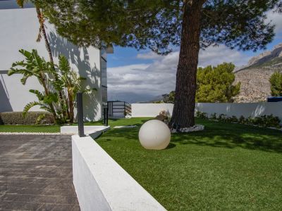 El exterior de la villa presenta una entrada pavimentada, césped artificial con un pino maduro, una moderna luz esférica y vistas a la montaña.