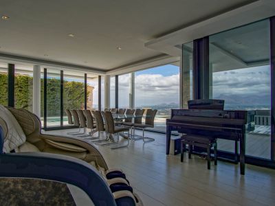 Espaciosa sala de estar y comedor con mesa de cristal para diez, piano de cola y sillón de masaje. Grandes ventanales ofrecen vistas panorámicas a la montaña y al paisaje.