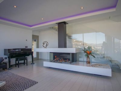 La elegante sala de estar presenta una moderna chimenea de gas transparente, un piano de cola y una escalera de cristal, con vistas a la montaña.
