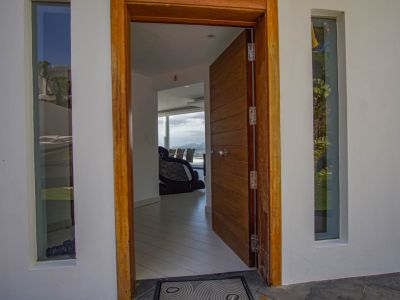 La entrada principal abierta revela una puerta de madera panelada y marco, flanqueada por ventanas verticales, con una visión del interior moderno y vistas a la montaña.