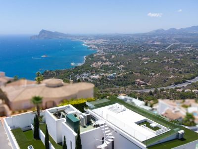 Vista aérea de la terraza en la azotea de la villa con escalera de caracol blanca, césped artificial, barandillas de cristal y vistas panorámicas al mar Mediterráneo y la costa.