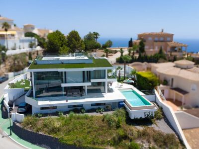 Vista aérea de la villa moderna de diseño blanco con techo verde, piscina infinita y jacuzzi separado, en un entorno con vistas al mar.