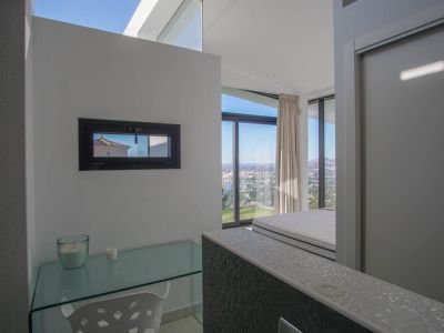 Zona de estudio con escritorio de cristal y ventana horizontal, ofreciendo vistas panorámicas al mar y la ciudad desde el dormitorio adyacente.