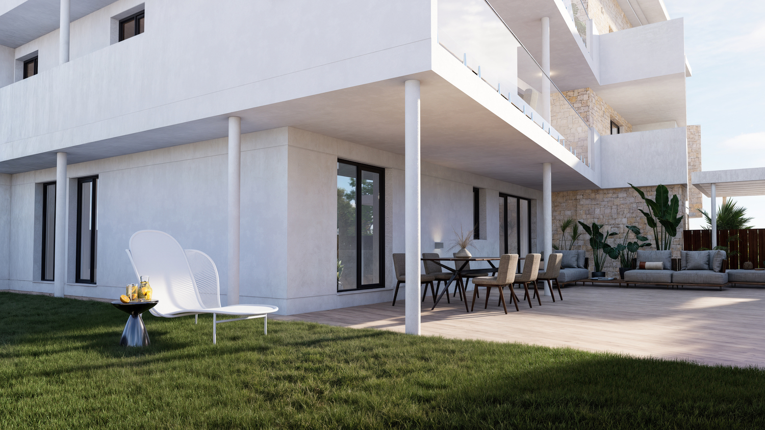 Amplia terraza en planta baja con tarima de madera clara, mobiliario de comedor y zona lounge, conectando con un cuidado césped que incluye una moderna tumbona blanca.