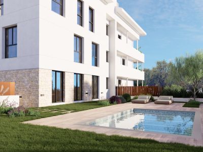 Edificio de apartamentos moderno con fachada blanca y base de piedra. Dispone de un jardín privado con piscina rectangular, pavimento de madera clara y dos tumbonas contemporáneas entre vegetación mediterránea.