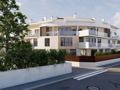 Edificio de apartamentos moderno con fachada curva, revestido de estuco blanco y piedra natural, con balcones acristalados. Vegetación mediterránea enmarca la propiedad desde la calle.