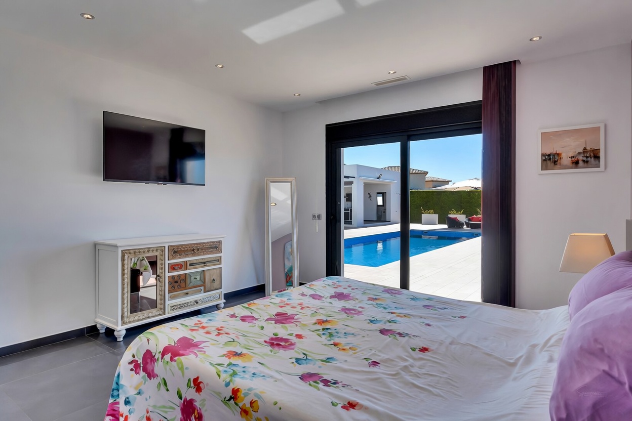 Amplio dormitorio con acceso directo a la piscina y terraza mediante puertas correderas, decorado con un edredón floral, TV y una cómoda singular.