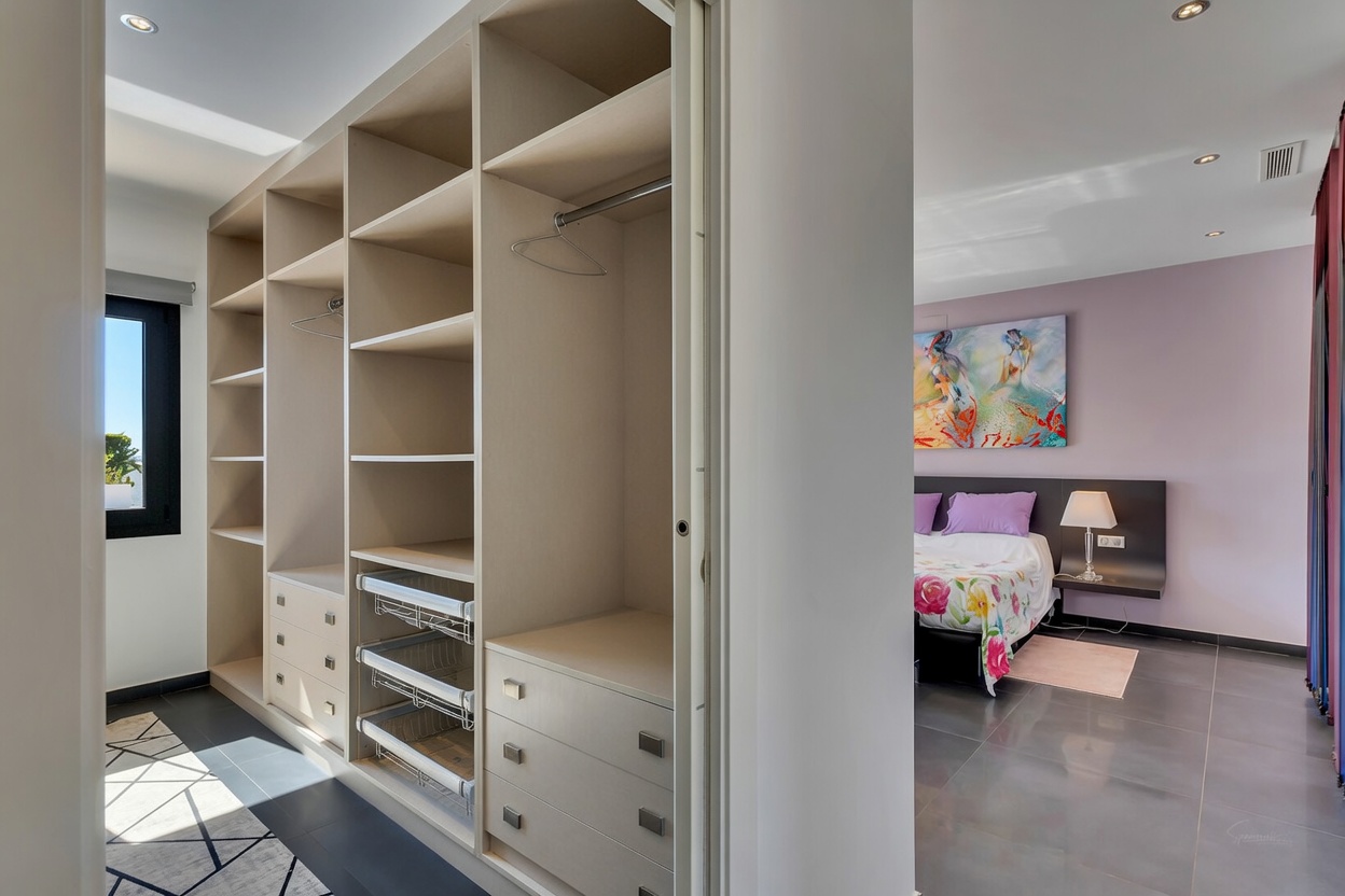 Amplio vestidor con estantes integrados, cajones y cestas extraíbles, conectado a un dormitorio con paredes lavanda y arte mural.