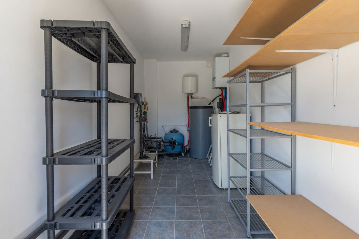 Cuarto de servicio con suelo de baldosas, estanterías variadas y equipamiento esencial como calentador de agua y bomba de piscina.