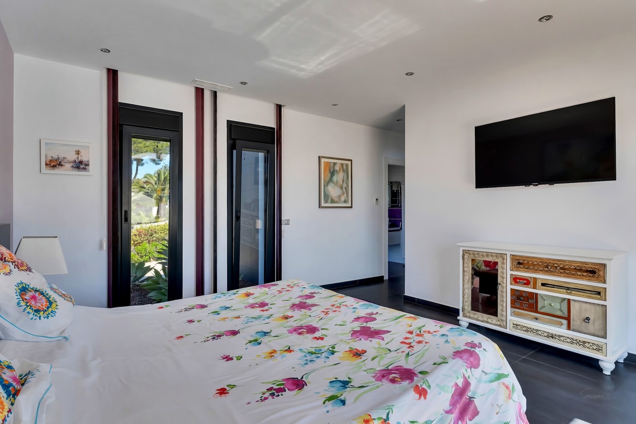Dormitorio luminoso con cama de diseño floral, acceso directo al jardín a través de puertas acristaladas y una singular cómoda de cajones variados.