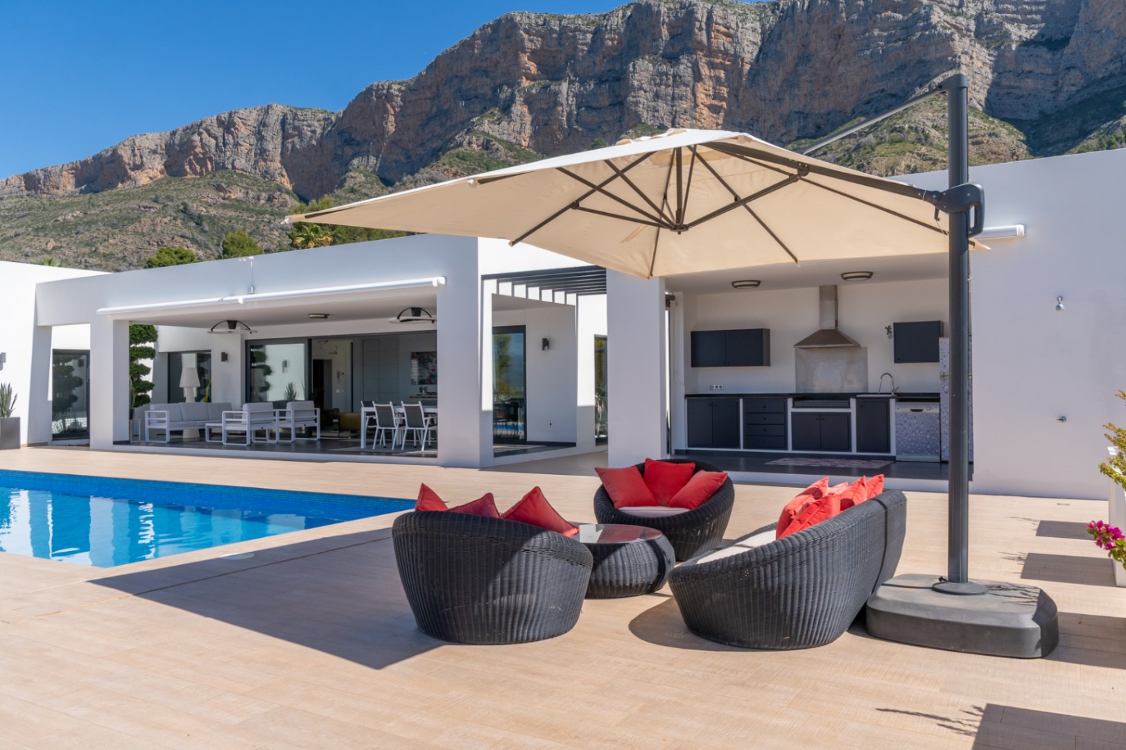 Espaciosa terraza con piscina, zona lounge y cocina exterior equipada, enmarcada por la imponente montaña del Montgó bajo un cielo azul.