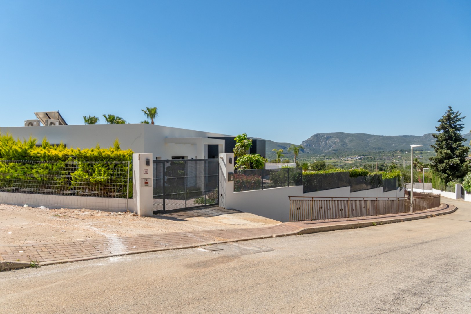 Fachada exterior de la villa moderna con portón de acceso, setos verdes y vistas a la montaña del Montgó desde la calle.