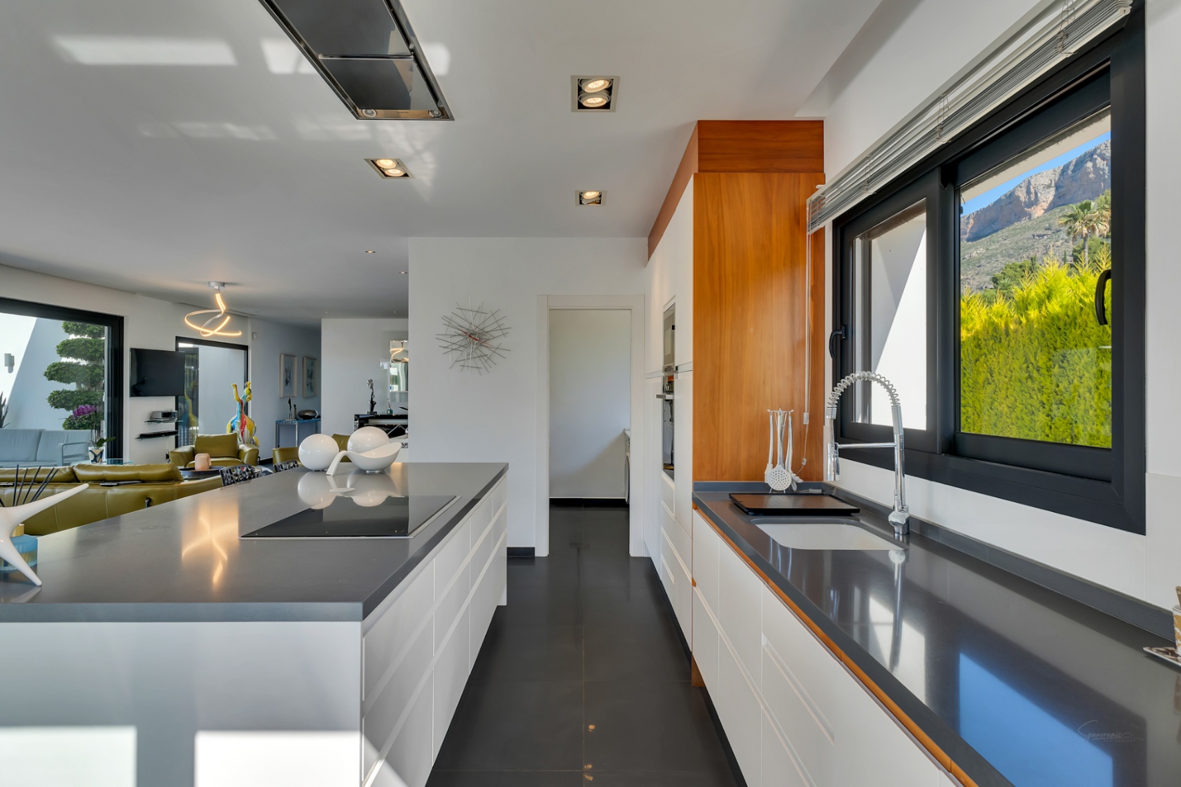 Moderna cocina de planta abierta con encimeras de cuarzo gris, armarios blancos sin tiradores, placa de inducción integrada en la isla y vistas a la montaña desde la ventana.
