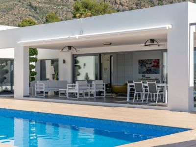 Amplia terraza cubierta con toldo retráctil, mobiliario de exterior y comedor, conectada a la piscina y al interior con vistas a la montaña.