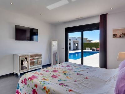 Amplio dormitorio con acceso directo a la piscina y terraza mediante puertas correderas, decorado con un edredón floral, TV y una cómoda singular.