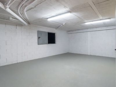 Amplio espacio inferior diáfano con paredes de bloques blancos, suelo gris claro y techo con instalaciones vistas, iluminado por luces fluorescentes.