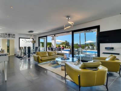 Amplio salón-comedor de planta abierta con acceso directo a la terraza y piscina climatizada mediante grandes puertas correderas. Mobiliairo verde oliva y suelo de gres oscuro.