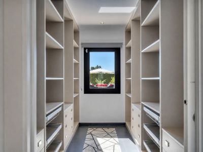 Amplio vestidor con estanterías integradas, cajones y cestas extraíbles, iluminado por luz natural de una ventana con vistas al jardín privado.