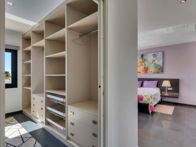 Amplio vestidor con estantes integrados, cajones y cestas extraíbles, conectado a un dormitorio con paredes lavanda y arte mural.