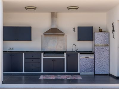Cocina exterior cubierta con armarios grises, encimera negra, fregadero, campana extractora y electrodomésticos integrados, ideal para barbacoas al aire libre.