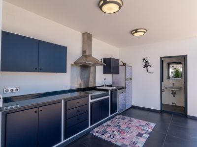 Cocina exterior de barbacoa con armarios azul oscuro, encimeras de piedra oscura, electrodomésticos de acero inoxidable y un práctico baño independiente adyacente.