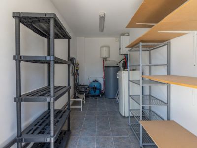 Cuarto de servicio con suelo de baldosas, estanterías variadas y equipamiento esencial como calentador de agua y bomba de piscina.