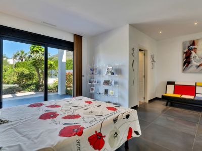 Dormitorio con grandes puertas correderas de cristal que abren a un jardín mediterráneo exuberante, suelo de gres oscuro y mobiliario contemporáneo.