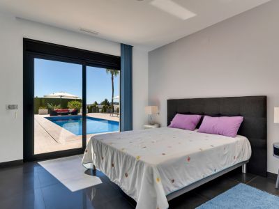 Dormitorio con suelos de baldosas oscuras y acceso directo a la piscina, que incluye una zona de relax exterior con sofá rojo y sombrilla bajo un cielo despejado.