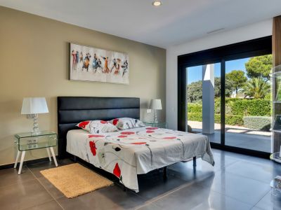Dormitorio luminoso con acceso directo al jardín a través de grandes puertas correderas, suelo de gres oscuro y mesitas de cristal.