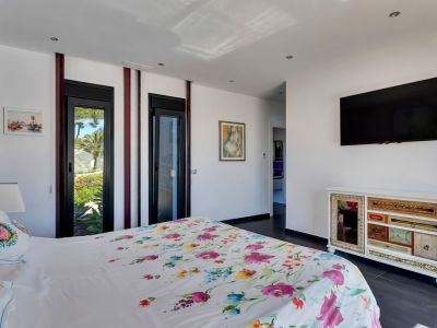 Dormitorio luminoso con cama de diseño floral, acceso directo al jardín a través de puertas acristaladas y una singular cómoda de cajones variados.