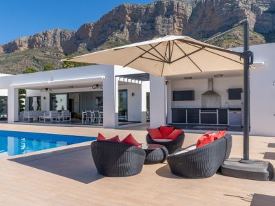 Espaciosa terraza con piscina, zona lounge y cocina exterior equipada, enmarcada por la imponente montaña del Montgó bajo un cielo azul.