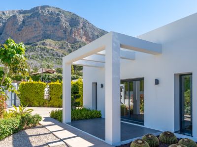 Exterior moderno con pérgola blanca, jardín mediterráneo y vistas despejadas a la majestuosa montaña del Montgó bajo un cielo azul.