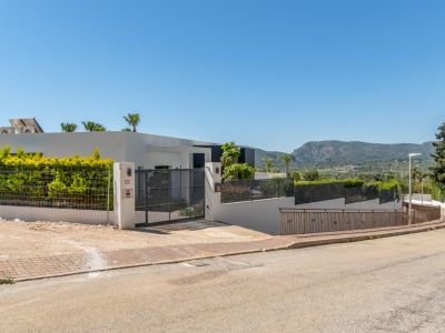 Fachada exterior de la villa moderna con portón de acceso, setos verdes y vistas a la montaña del Montgó desde la calle.